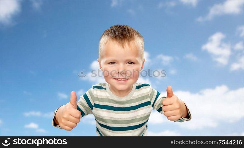 childhood, gesture and people concept - portrait of smiling little boy in striped shirt showing thumbs up over blue sky and clouds background. smiling boy in striped shirt showing thumbs up