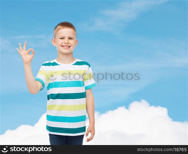 childhood, gesture and people concept - smiling little boy in casual clothes making ok gesture over blue sky background