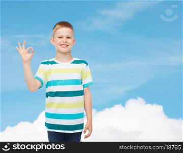 childhood, gesture and people concept - smiling little boy in casual clothes making ok gesture over blue sky background