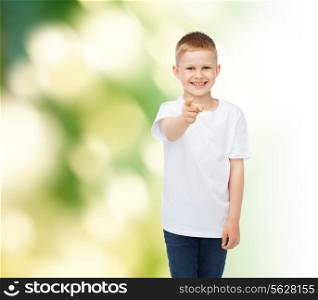 childhood, gesture, ecology, advertisement and people concept - smiling boy in white t-shirt pointing finger at you over green background