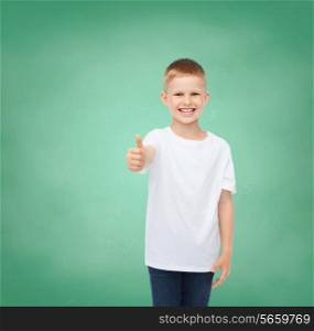 childhood, gesture, education, advertisement and people concept - smiling boy in white t-shirt showing thumbs up over green board background