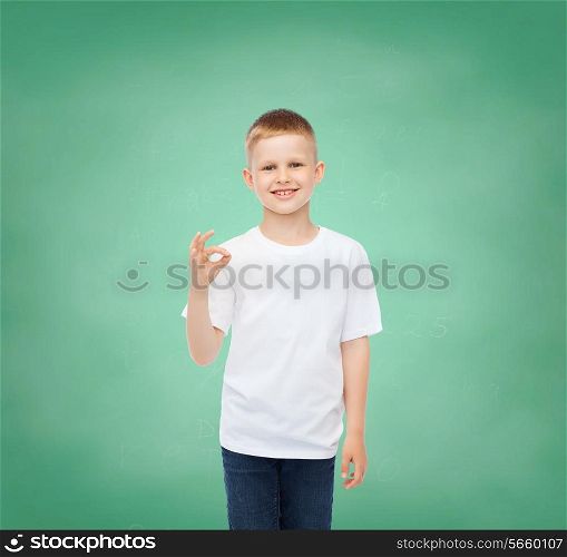 childhood, gesture, education, advertisement and people concept - smiling boy in white t-shirt showing ok sign over green board background