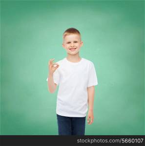 childhood, gesture, education, advertisement and people concept - smiling boy in white t-shirt showing ok sign over green board background