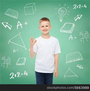 childhood, gesture, education, advertisement and people concept - smiling boy in white t-shirt showing ok sign over green board with doodles background