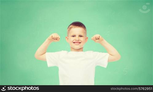 childhood, gesture, education, advertisement and people concept - smiling boy in white t-shirt flexing biceps over green board background