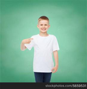 childhood, gesture, education and advertisement concept - smiling boy in t-shirt pointing his finger at himself over green board background