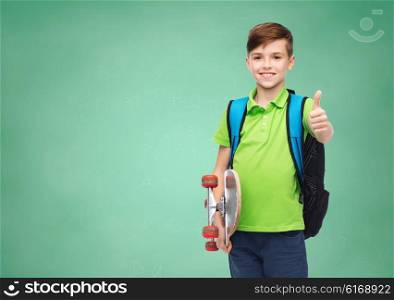 childhood, gesture, education and people concept - happy smiling student boy with backpack and skateboard showing thumbs up over green school chalk board background