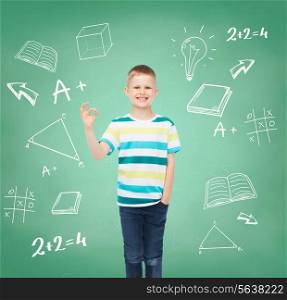 childhood, gesture, education and people concept - smiling little boy in casual clothes making OK gesture over green board with doodles background