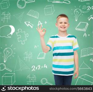 childhood, gesture, education and people concept - smiling little boy in casual clothes making OK gesture over green board with doodles background
