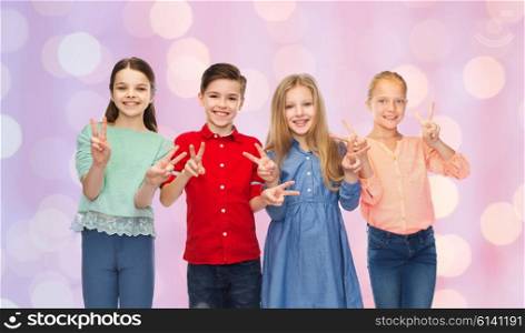 childhood, gesture, friendship and people concept - happy smiling boy and girls showing peace hand sign over pink holidays lights background