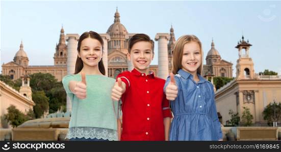 childhood, gesture, travel, tourism and people concept - happy smiling boy and girls showing thumbs up over national museum of barcelona background