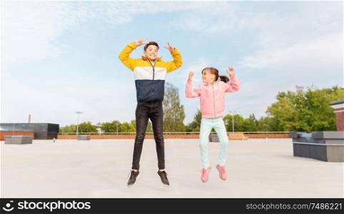 childhood, happiness and fun concept - happy children or brother and sister jumping on rooftop and showing peace gesture. happy children jumping on roof and showing peace
