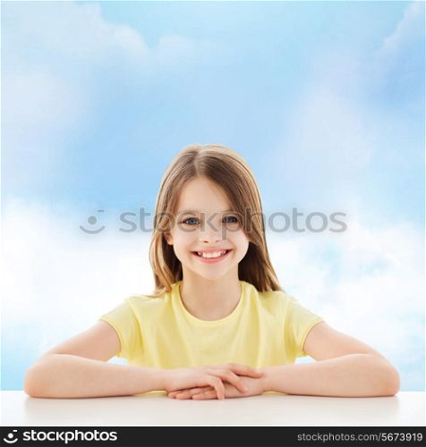 childhood, happiness and people concept - beautiful little girl sitting at table over cloudy sky background