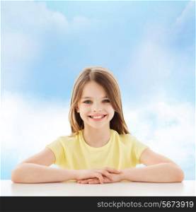 childhood, happiness and people concept - beautiful little girl sitting at table over cloudy sky background