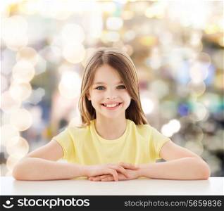 childhood, happiness, holidays and people concept - beautiful little girl sitting at table over sparkling background