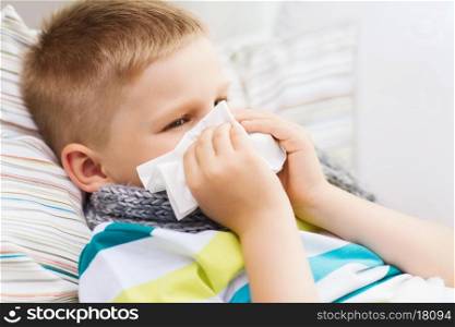 childhood, healthcare and medicine concept - ill boy with flu blowing nose at home