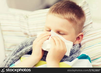 childhood, healthcare and medicine concept - ill boy with flu blowing nose at home