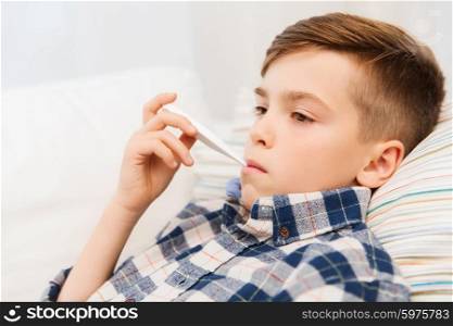 childhood, healthcare and medicine concept - ill boy with flu measuring temperature by thermometer at home