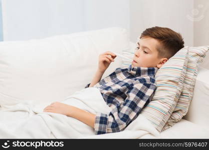 childhood, healthcare and medicine concept - ill boy with flu measuring temperature by thermometer at home