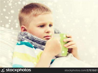 childhood, healthcare and people concept - ill boy with flu in bed drinking from cup at home
