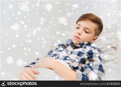 childhood, healthcare, people and medicine concept - ill boy with flu lying in bed at home over snow