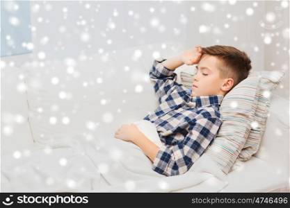 childhood, healthcare, people and medicine concept - ill boy with flu lying in bed at home and suffering from headache over snow