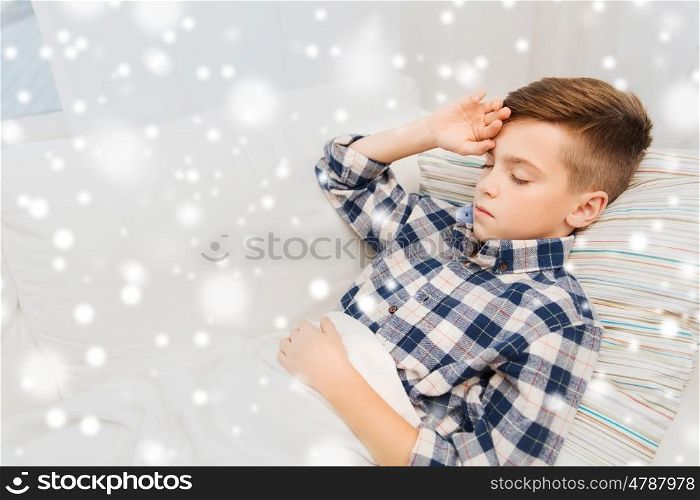 childhood, healthcare, people and medicine concept - ill boy with flu lying in bed at home and suffering from headache over snow