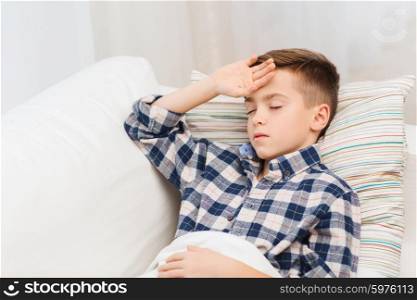 childhood, healthcare, people and medicine concept - ill boy with flu lying in bed at home and suffering from headache