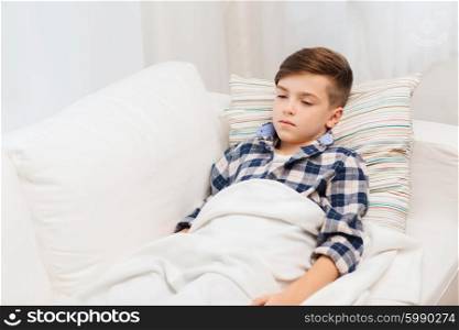 childhood, healthcare, people and medicine concept - ill boy with flu lying in bed at home