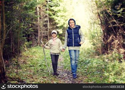childhood, hiking, family, friendship and people concept - two happy kids walking along forest path