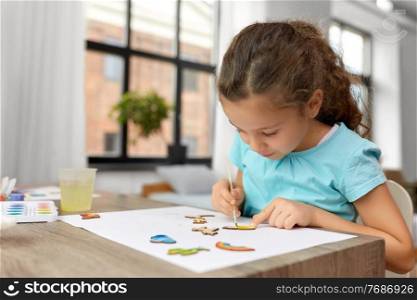 childhood, hobby and leisure concept - little girl with brush painting wooden chipboard items at home. little girl painting wooden items at home