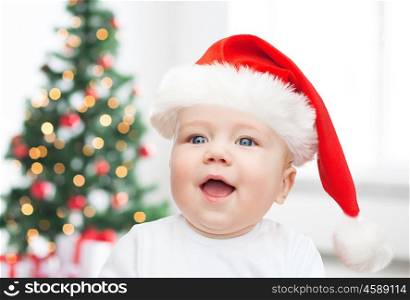 childhood, holidays and people concept - beautiful little baby boy in christmas santa hat over living room with christmas thee lights background