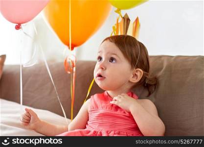 childhood, holidays and people concept - happy baby girl air balloons wearing princess crown on birthday party at home. happy baby girl in crown on birthday party at home