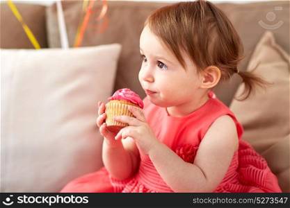 childhood, holidays and people concept - happy baby girl eating cupcake on birthday party at home. happy baby girl eating cupcake on birthday party