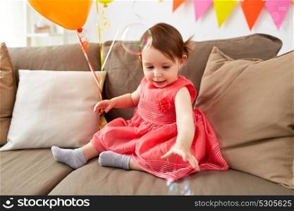 childhood, holidays and people concept - happy baby girl playing with soap bubbles on birthday party at home. baby girl with soap bubbles on birthday party