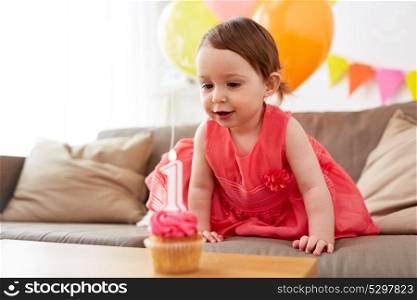 childhood, holidays and people concept - happy baby girl with cupcake on birthday party at home. baby girl with birthday cupcake at home party