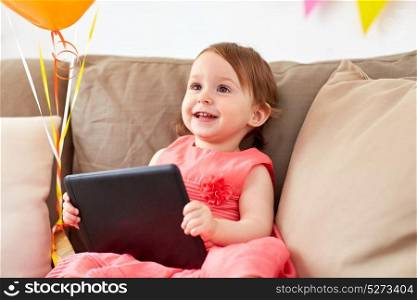 childhood, holidays and people concept - happy baby girl with tablet pc computer and air balloons on birthday party at home. baby girl with tablet pc on birthday party at home