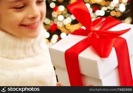 childhood, holidays and people concept - happy beautiful girl with christmas gift box over festive lights background. happy girl with christmas gift over festive lights