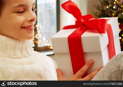childhood, holidays and people concept - happy beautiful girl with christmas gift box at home over festive lights background. happy beautiful girl with christmas gift at home