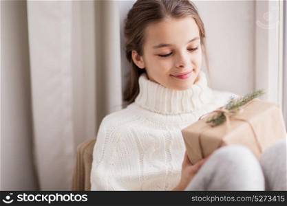childhood, holidays and people concept - happy beautiful girl with christmas gift sitting at home. girl with christmas gift sitting at home