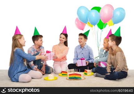 childhood, holidays, celebration, friendship and people concept - happy smiling children in party hats with cake giving presents at birthday party