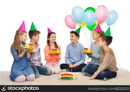 childhood, holidays, celebration, friendship and people concept - happy smiling children in party hats with birthday cake and balloons