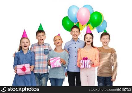 childhood, holidays, friendship and people concept - happy smiling children in party hats with gifts and balloons on birthday