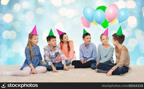 childhood, holidays, friendship and people concept - happy smiling children in party hats on birthday over blue holidays lights background