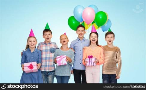 childhood, holidays, friendship and people concept - happy smiling children in party hats with gifts and balloons on birthday over blue background