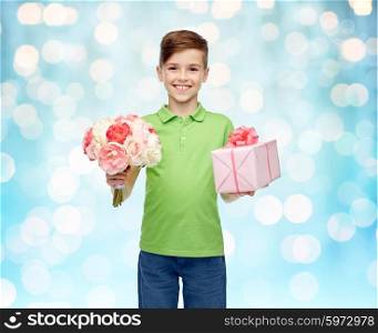 childhood, holidays, presents and people concept - happy boy holding flower bunch and gift box over blue lights background