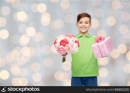 childhood, holidays, presents and people concept - happy boy holding flower bunch and gift box over lights background