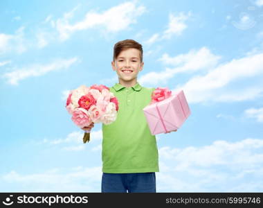 childhood, holidays, presents and people concept - happy boy holding flower bunch and gift box over blue sky and clouds background