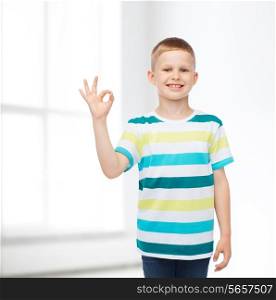 childhood, home, gesture and people concept - smiling little boy in casual clothes making ok gesture over white room background