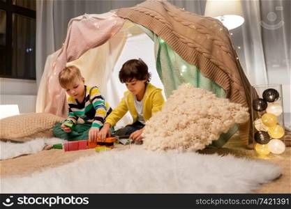 childhood, hygge and friendship concept - boys playing toy blocks in kids tent or teepee at home. boys playing toy blocks in kids tent at home